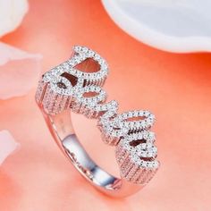 Elevate your style with our stunning 925 sterling silver Barbie ring. This exquisite piece features the word “Barbie” elegantly crafted in sparkling gemstones, creating a dazzling and glamorous accessory perfect for any fashion-forward individual. The ring’s intricate design and shimmering details make it a standout piece in any jewelry collection. Shipping:Takes 5-8 business days depending on stock, these beautiful rings are custom sized and made in small batches. If your size is in stock this item will ship immediately Product Details: Material: 925 Sterling Silver Gemstones: Clear Cubic Zirconia Design: Sparkling “Barbie” lettering Finish: Polished Size: Adjustable Occasion: Everyday wear, parties, and special occasions Why Choose This Ring? Elegance: The combination of sterling silver Luxury Sparkling Rings For Party, Luxury Sparkling Party Rings, Elegant Silver Diamond Ring For Party, Dazzling Sterling Silver Jewelry For Promise, Dazzling Sterling Silver Promise Jewelry, Pave Setting Crystal Promise Ring, Party Rings With Pave Setting In Diamond White, Dazzling Diamond Ring With Pave Setting For Party, Dazzling Silver Jewelry For Promise