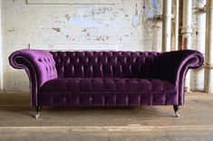 a purple couch sitting in front of a white brick wall with exposed pipes on it