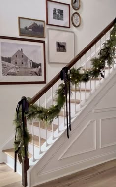 the stairs are decorated with christmas garlands and pictures on the wall above them, along with wreaths hanging from the banister