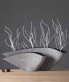 two metal bowls with branches in them on a wooden table, against a gray background