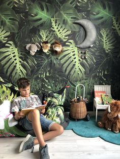 a young boy sitting on the floor reading a book in front of a jungle wallpaper