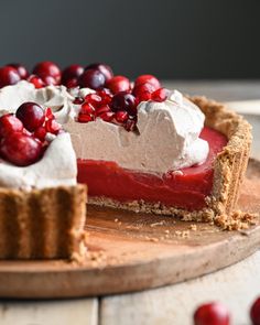 a pie with cranberries and whipped cream on top sitting on a wooden board