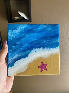 a person holding up a small painting with a starfish on it's side