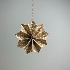 an origami flower hanging from a string on a gray background with white dots