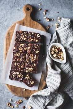 a wooden cutting board topped with brownies and nuts