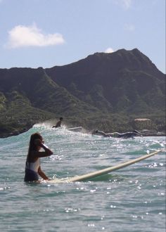 a woman riding on top of a surfboard in the ocean next to a mountain