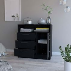 a black cabinet with three drawers in a room next to a bed and potted plant