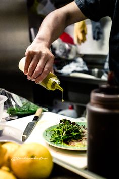 a person pouring dressing onto a plate with lemons and other food on the table