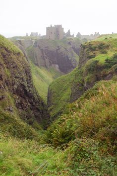 an old castle perched on top of a cliff in the middle of a green valley