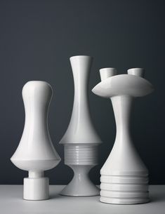 three white vases sitting next to each other on top of a table in front of a gray wall