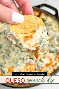 a hand holding a tortilla chip over a skillet filled with spinach dip