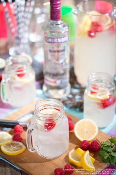 some lemons and raspberries are sitting on a cutting board next to drinks