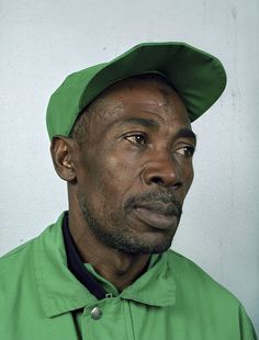 a man in a green shirt and hat looking off to the side with a serious look on his face