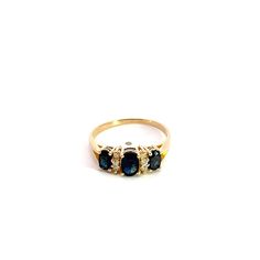 three stone ring in yellow gold with blue and white stones on the sides, set against a white background