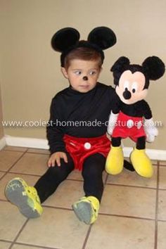 a little boy sitting on the floor with a mickey mouse stuffed animal in front of him