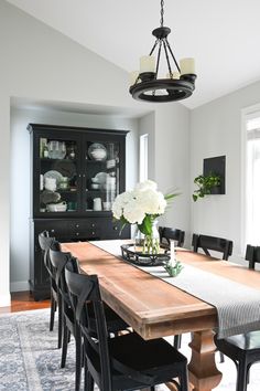 the dining room table is set with black chairs and white flowers in a glass vase