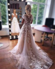 a woman standing in front of a mirror wearing a wedding dress with flowers on it