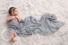 a baby wrapped in a blanket laying on top of a fluffy white rug with her hands under her chin