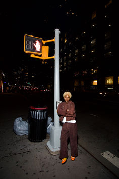 a person sitting on a pole next to a street sign and trash can at night