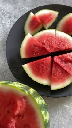 slices of watermelon on a black plate next to another piece of watermelon