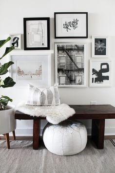 a living room with pictures on the wall and a white pouffle ottoman in front of it