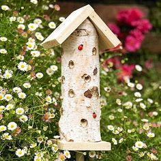 a bird house made out of wood with holes in the side and flowers around it