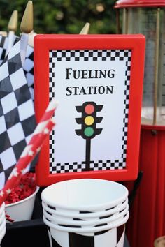 a table topped with lots of white plates and buckets filled with red flowers next to a sign that says fueling station