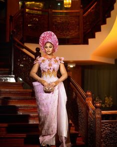 a woman wearing a pink dress and headpiece standing on stairs with her hands in her pockets