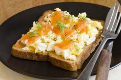 a black plate topped with two pieces of toast covered in scrambled eggs and carrots