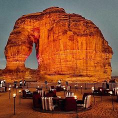 an outdoor dining area in front of a large rock formation with candles lit up on it