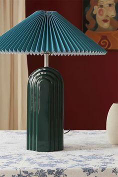 a green lamp sitting on top of a table next to a white vase and painting