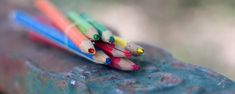 three colored pencils sitting on top of a piece of blue metal with green and yellow tips