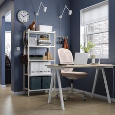 a desk with a laptop on it in front of a window and clock mounted to the wall