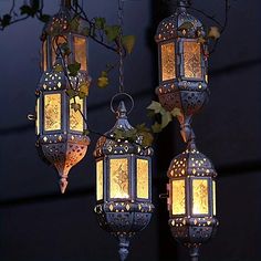 three hanging lanterns are lit up in the dark with ivy growing on them and one light is turned on