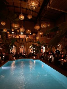 an indoor swimming pool surrounded by chandeliers and hanging lights with people sitting around it