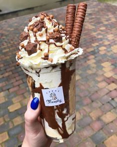 a person holding up an ice cream sundae with chocolate and marshmallows