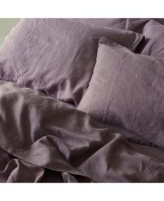 an unmade bed with purple sheets and pillows