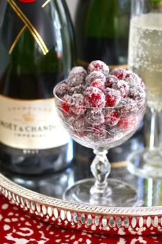 a glass bowl filled with raspberries next to two bottles of champagne