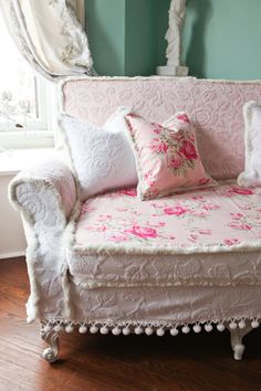 a white couch with pink flowers on it in front of a large mirror and wooden floor