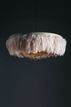 a light fixture with feathers hanging from it's sides in a dark room, against a black background