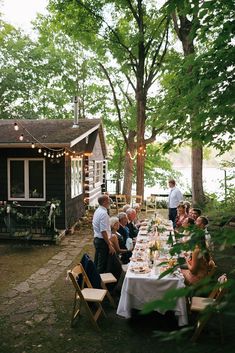 a group of people sitting around a table in front of a house with lights on it