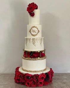 a three tiered wedding cake with red roses on the bottom and gold trimmings