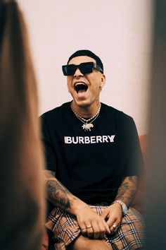 a man with his mouth wide open sitting on a chair wearing sunglasses and a t - shirt that says burberry