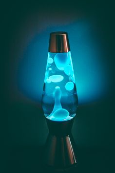 a glass vase with blue liquid in it on a black surface and lit up by the light