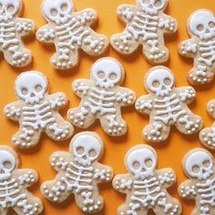 several decorated sugar cookies with white frosting on an orange tablecloth, one is shaped like a skeleton and the other looks like a human skull