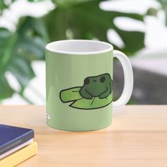 a green coffee mug with an image of a frog on it's side sitting on a table