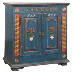 an old blue cabinet with flowers painted on the front and sides, sitting against a white background