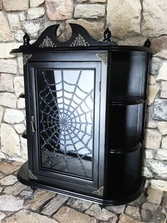 a black cabinet with a spider web design on the front and side doors, sitting against a stone wall