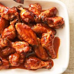 a white plate topped with chicken wings covered in bbq sauce next to a fork