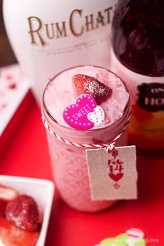 a pink drink with strawberries in it next to a bottle of rumchat